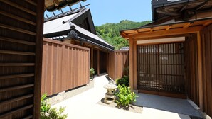 A traditional Japanese garden with wooden fences, a stone lantern, and a view of a forested hill. - SATOYAMA HOTEL KANENONE TAMBA (Tamba)