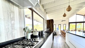 A modern kitchen with a gas stove, white cabinets, and large windows. - Hare Mahatu (Hanga Roa)