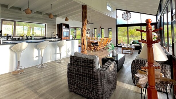A spacious living area with a large dining table, wicker furniture, and a view of the outdoors. - Hare Mahatu (Hanga Roa)