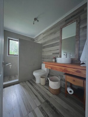 A bathroom with a wooden vanity, a toilet, a shower, and a window.