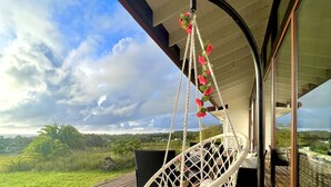 A wicker chair on a wooden deck with a view of a grassy landscape and a cloudy sky. - Hare Mahatu (Hanga Roa)