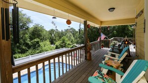 Eine Holzterrasse mit Pool, Gartenmöbeln und Blick auf Bäume.