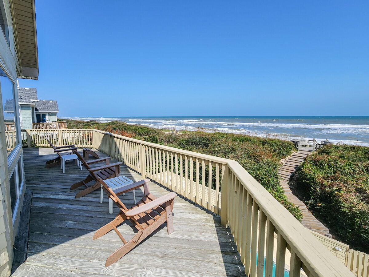 A wooden deck with lounge chairs and a view of the ocean.
