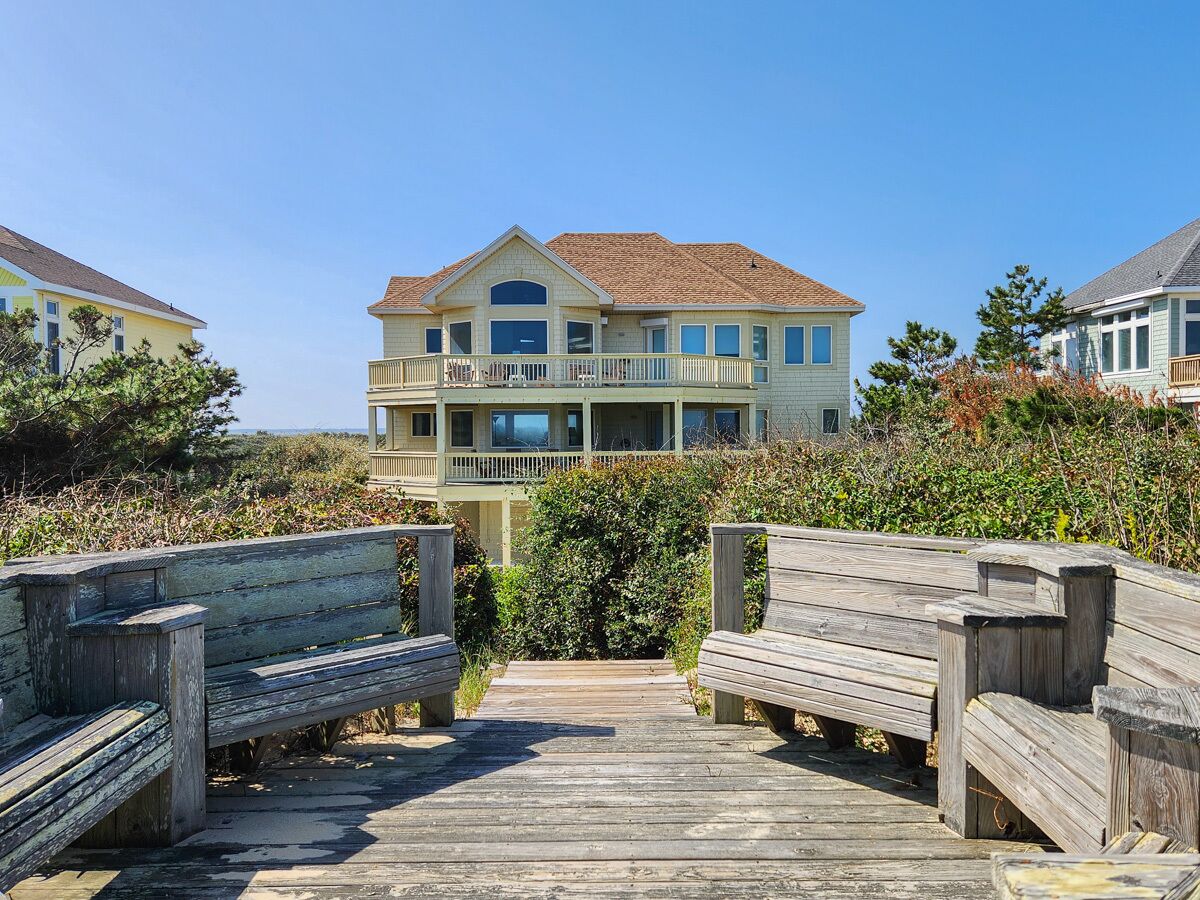 A beachfront property with a wooden boardwalk leading to a two-story house with a balcony.