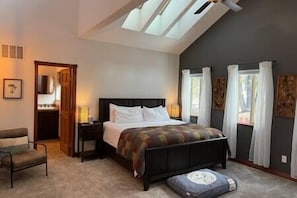 A bedroom with a bed, a chair, a nightstand, a lamp, and a window with curtains.