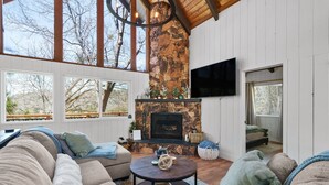 A cozy living room with a stone fireplace, large windows, and a comfortable seating area.