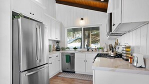 A modern kitchen with white cabinetry, stainless steel appliances, and a view of the outdoors through a window.