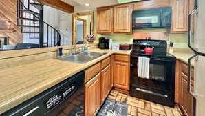 Una cocina con armarios de madera, un lavamanos de acero inoxidable, una estufa negra y un microondas.