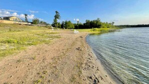 Una propiedad a orillas del río, con playa de arena, una fila de sillas blancas y un edificio al fondo.
