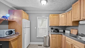A compact kitchen with wooden cabinets, a white refrigerator, a microwave, a sink, and a window with blinds. - Pet Friendly 1BR in Ohio City (Cleveland)