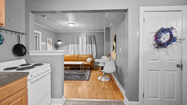 A kitchen with a stove, a dining area with a table and chairs, a sofa, and a door with a wreath. - Pet Friendly 1BR in Ohio City (Cleveland)