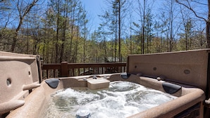 A hot tub with a wooden deck and a view of a forest.
