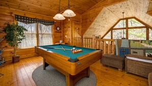 A wooden interior with a pool table, a clock, and a large window.