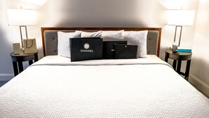 A neatly made bed with a white comforter and pillows, two bedside tables with lamps, and two Chanel bags placed on the bed. - Spacious Studio near Downtown LA (Los Angeles)