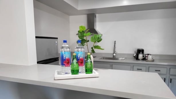 A modern kitchen with a white countertop, a sink, and a coffee machine. There are three bottles of Fiji water on the counter. - Spacious Studio near Downtown LA (Los Angeles)