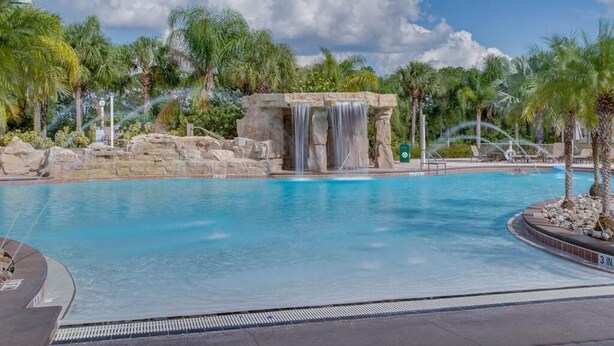 Ein Pool mit Wasserfall, umgeben von Palmen und blauem Himmel.