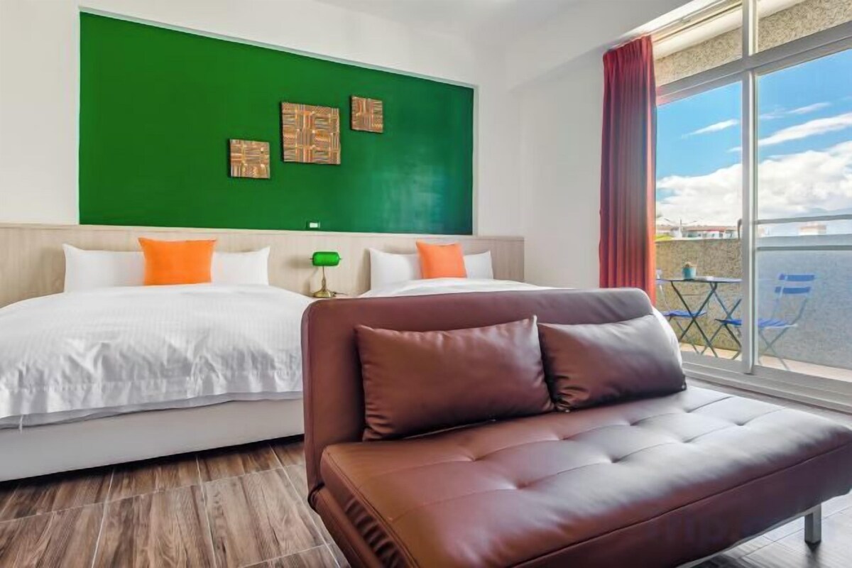 Habitación de hotel con cama, sofá, pared verde y vista al mar.