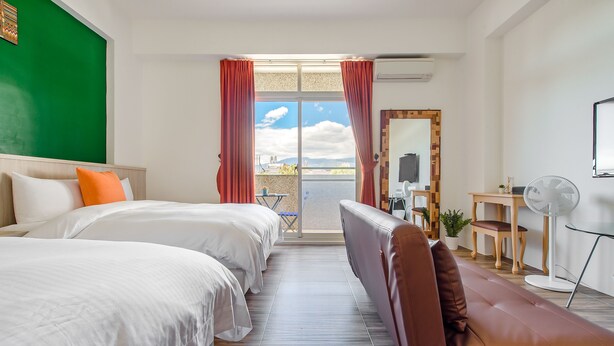 Habitación de hotel con dos camas, un sofá, un balcón con vistas, un escritorio y un ventilador.