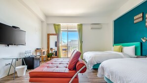 Una habitación de hotel moderna con sofá, dos camas, televisor y balcón con vistas.