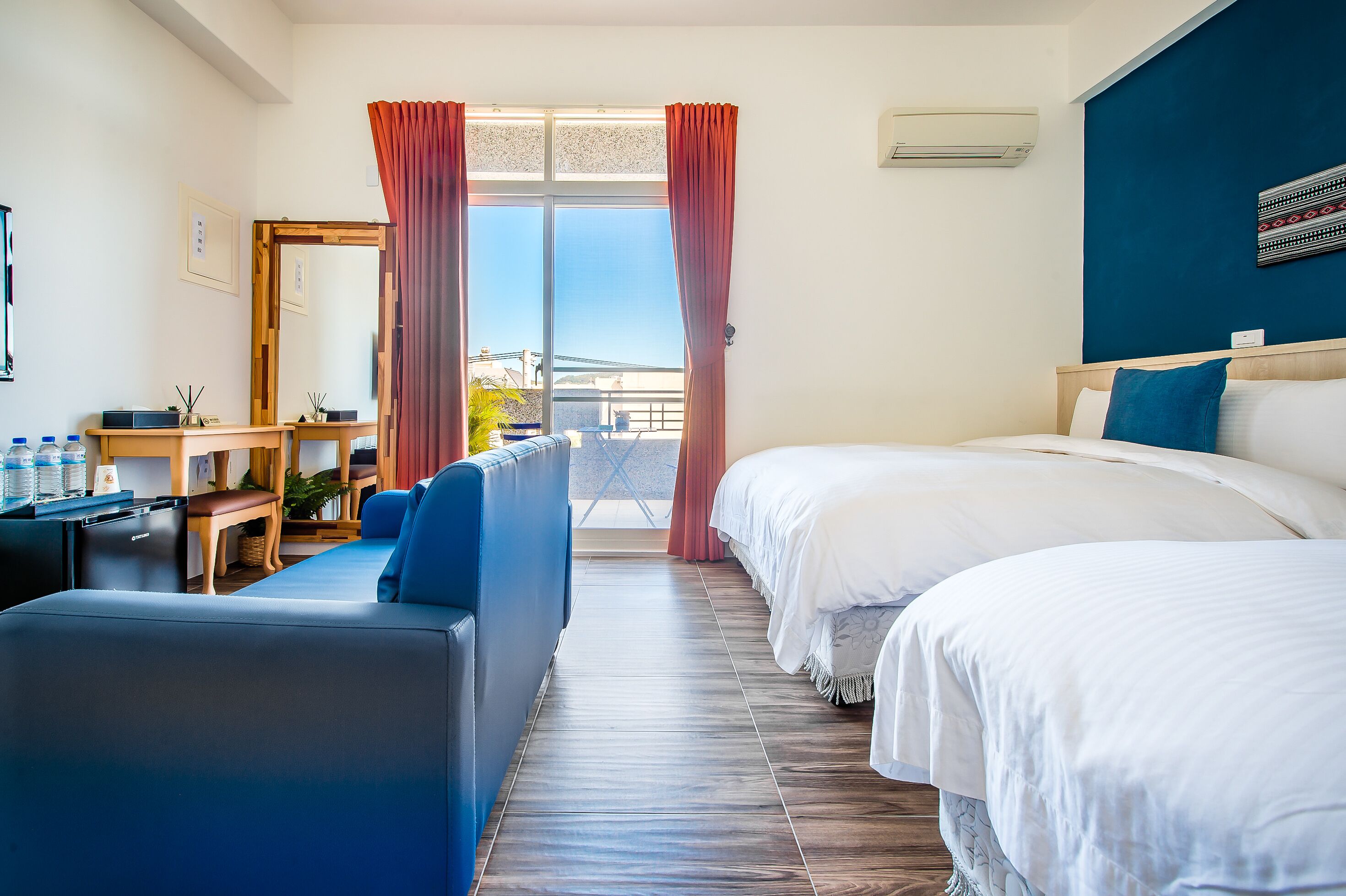 Habitación de hotel con cama, sofá, escritorio con computadora y ventana con cortinas.