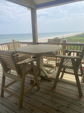 Eine Holzterrasse mit Tisch und Stühlen, mit Blick auf einen Strand.