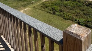 Terraza de madera con vista a una playa, olas y cielo despejado.