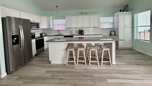 Una cocina moderna con armarios blancos, un refrigerador de acero inoxidable, una encimera de granito y taburetes de madera.
