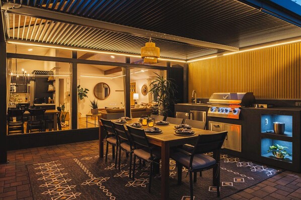 An outdoor dining area with a grill, a dining table set for four, and a patterned rug.