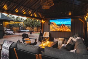 Un patio al aire libre con un brasero, asientos y una pantalla de televisión que muestra un paisaje desértico.