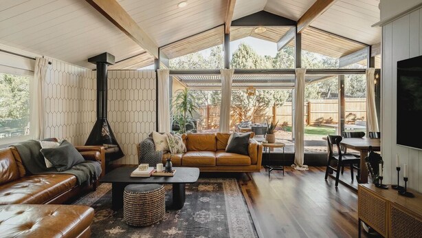 Amplia sala de estar con techo alto, chimenea, sofás de cuero, una mesa de centro y un gran ventanal con vistas al exterior.