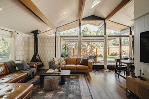 A spacious living room with a high ceiling, a fireplace, leather sofas, a coffee table, and a large window offering a view of the outdoors.