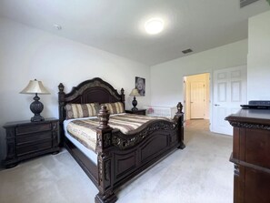 Une chambre à coucher avec un grand lit, deux tables de chevet, une commode et une porte donnant sur une autre pièce.