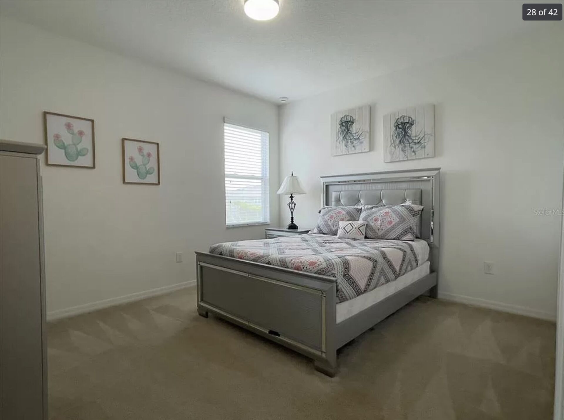 Ein Schlafzimmer mit Bett, Nachttisch, Fenster und Wandbildern.