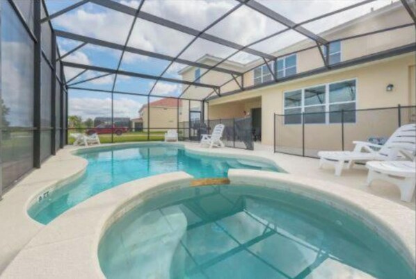Un espace piscine doté d’une enceinte en verre, de chaises longues et d’un bâtiment en arrière-plan.