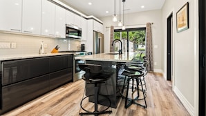 Una cocina moderna con armarios blancos, un refrigerador de acero inoxidable y una isla central con taburetes de bar.