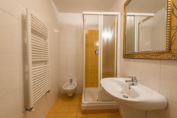 Une salle de bain avec un radiateur blanc, un bidet, un espace douche et un lavabo avec un miroir.