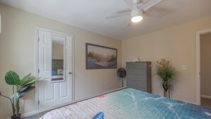 Un dormitorio con cama, puerta, ventilador, cómoda y planta.