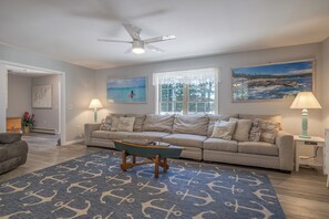 A living room with a beige sofa, a coffee table, a blue rug with anchor patterns, a ceiling fan, and two wall-mounted lamps. - Waterfront Hot Tub Kids Playscape Kayaks  Pet Friendly Mini Resort with A/C (Gouldsboro)
