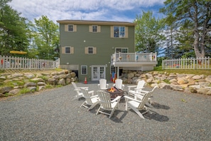 A two-story building with a balcony, surrounded by a white picket fence, and a fire pit with chairs in front. - Waterfront Hot Tub Kids Playscape Kayaks  Pet Friendly Mini Resort with A/C (Gouldsboro)