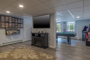 A home entertainment room with a flat-screen TV, a pool table, and a bookshelf filled with video games.