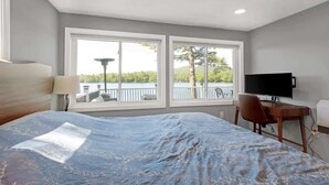 Une chambre à coucher comprenant un lit, un bureau, une télévision et de grandes fenêtres donnant sur un balcon et des arbres.