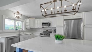 Une cuisine moderne avec des armoires blanches, des appareils en acier inoxydable, un îlot central et un luminaire suspendu.