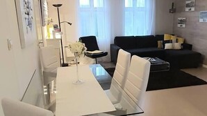 Un salon moderne avec une table à manger en verre, des chaises blanches, un canapé noir et une table basse.