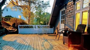 Une terrasse en bois avec des meubles d’extérieur, une bougie allumée et une maison en arrière-plan.