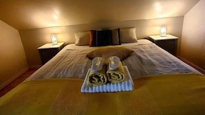 Un lit bien fait, avec un plateau contenant des serviettes pliées et une paire de chaussons, deux lampes de chevet et un oreiller posé sur la tête de lit.