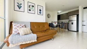 Un saló modern amb un sofà marró, una taula de menjador amb cadires i una zona de cuina amb un frigorífic.