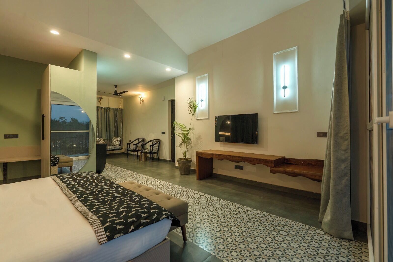 Une chambre moderne avec un lit, une télévision, un banc et un balcon équipé de chaises.