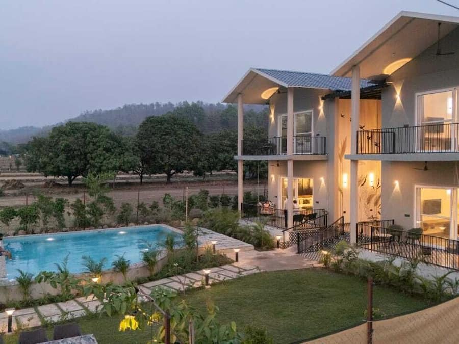 A two-story building with a swimming pool, surrounded by greenery and hills in the background.