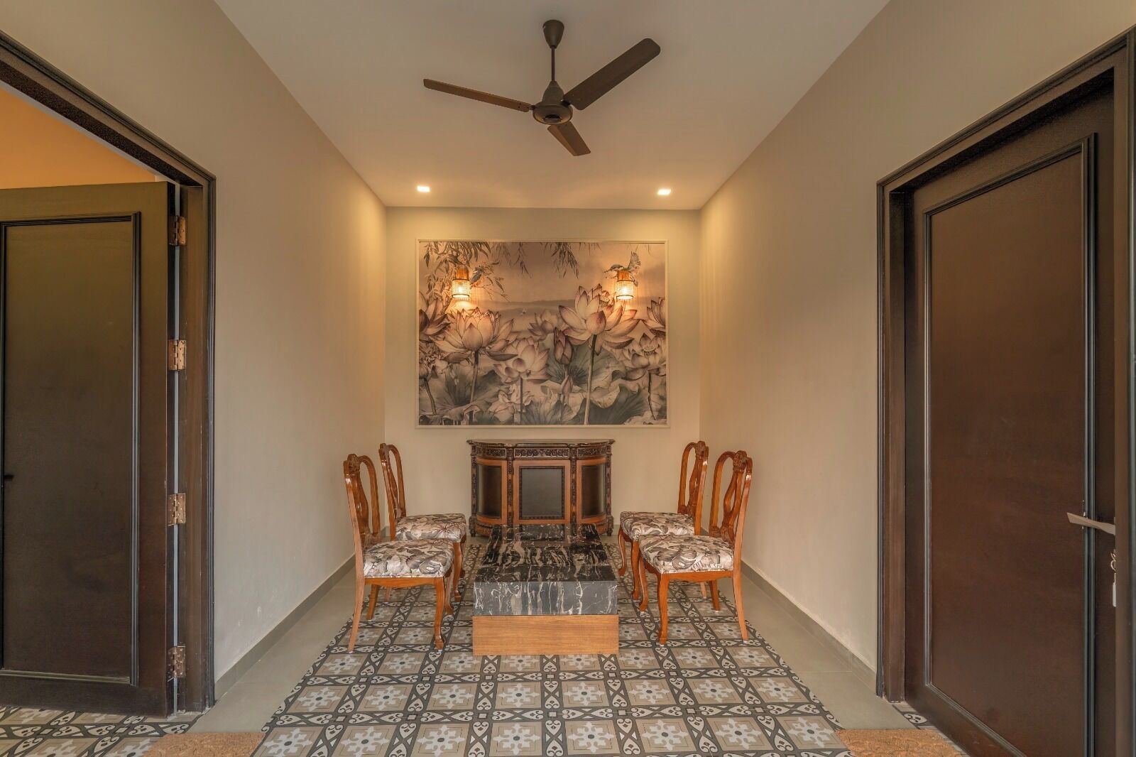 A hallway with a ceiling fan, a wall-mounted light fixture, and a framed artwork above a table with chairs.