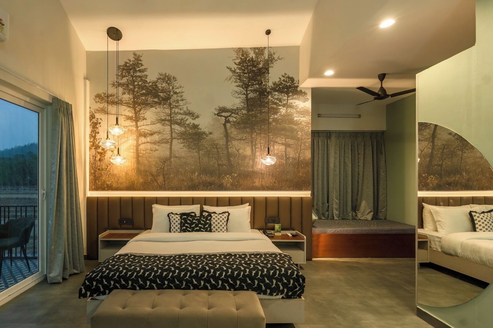 A modern bedroom with a large bed, a seating area, and a view of trees through a window.